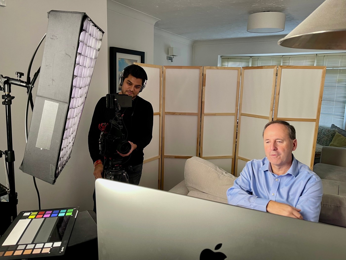 Nitesh operating camera behind the monitor on an interview shoot, with softbox lighting and a colour chart in frame